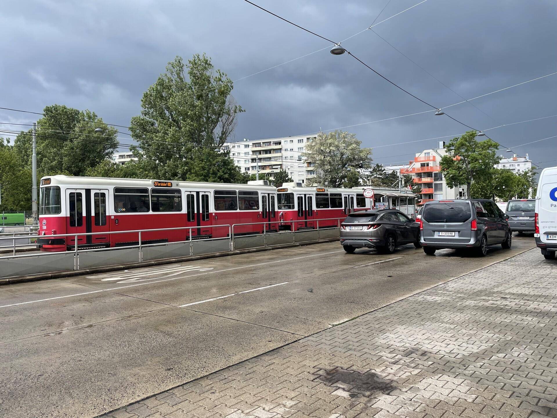 Eine Straßenansicht mit einer roten Straßenbahn, Autos und Wohngebäuden unter einem bewölkten Himmel.