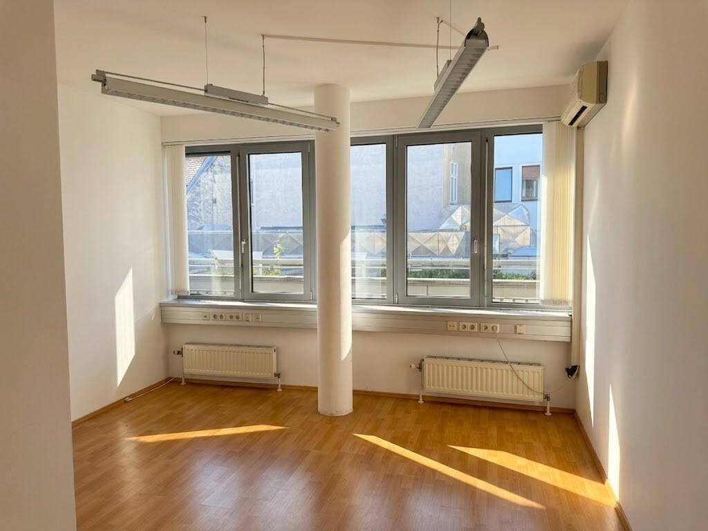 Helles Büro mit Laminatboden, großen Fenstern, Klimaanlage und einem zentralen Pfeiler.