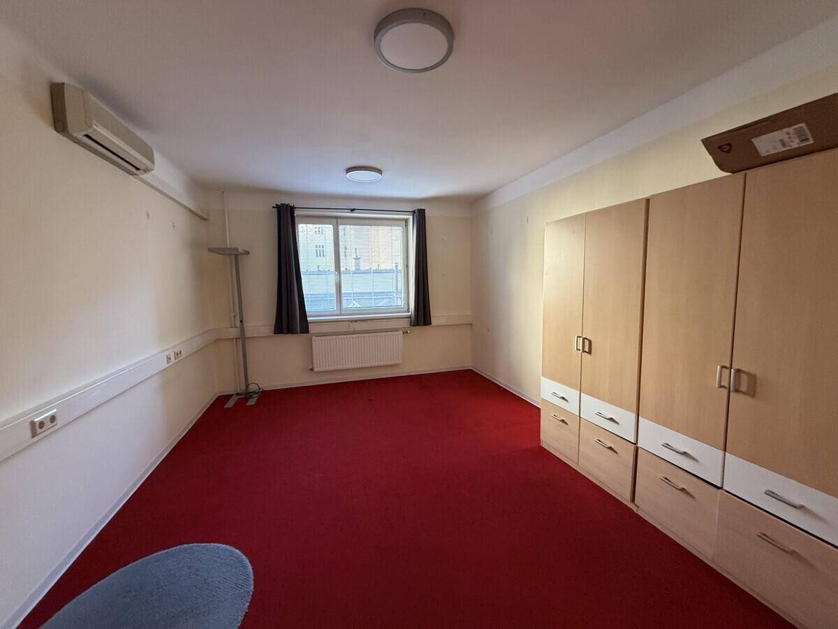 Kleines Büro mit rotem Teppichboden, einem Fenster und einem Einbauschrank an der Wand.