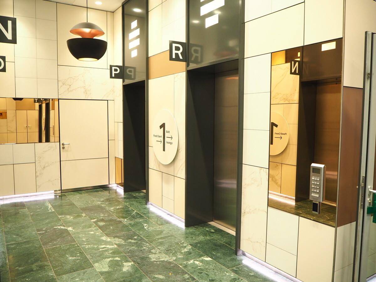 Moderner Aufzugsbereich mit grünen Marmorfliesen und hellen Wandpaneelen in einem Bürogebäude.