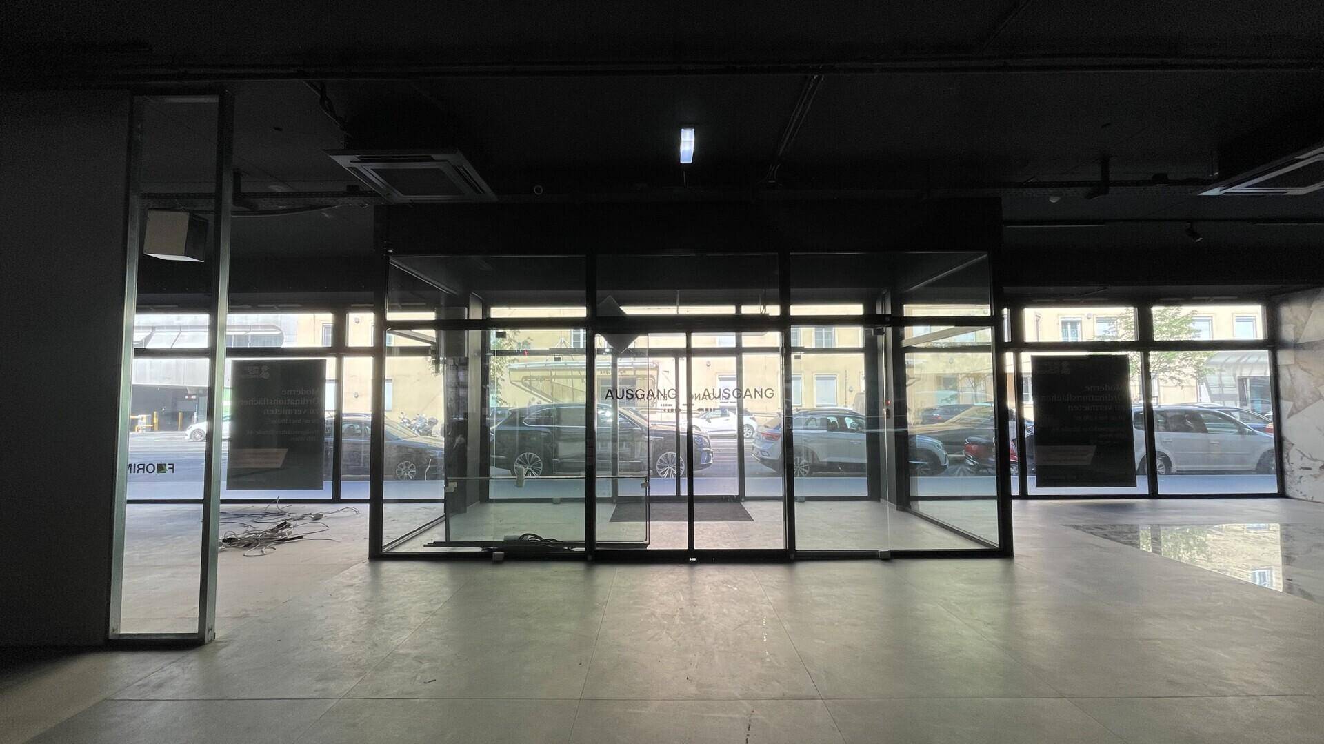 Innenansicht eines leeren Geschäftsraums mit breiter Glasfront und automatischen Schiebetüren.