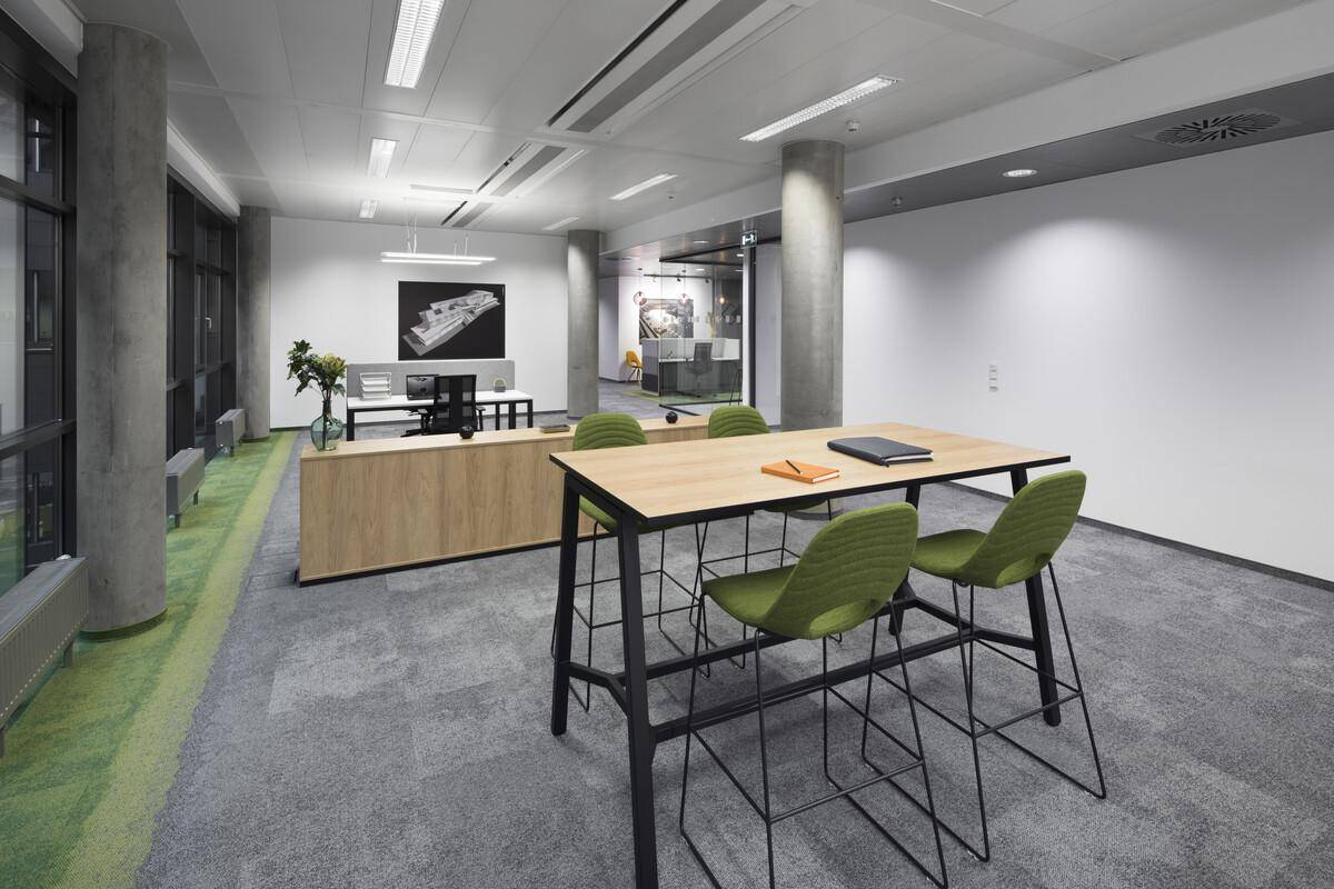 Geräumiger, offener Bürobereich mit verschiedenen Arbeits- und Besprechungszonen sowie großen Fenstern und Teppichboden.