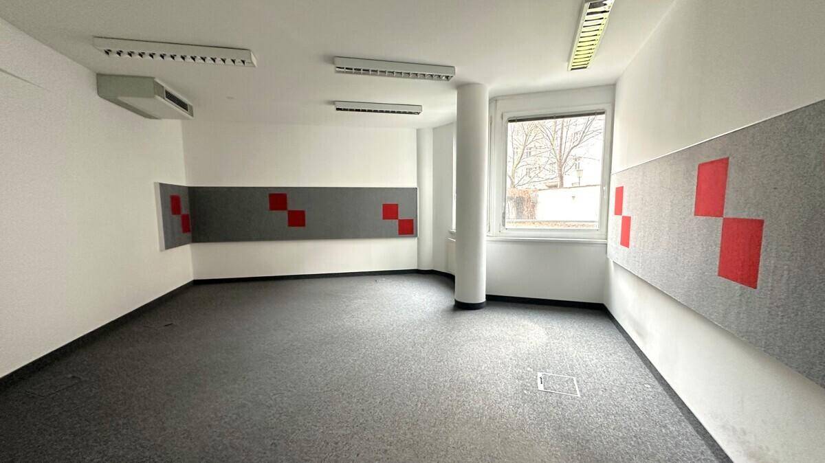 Bürofläche mit grauem Teppichboden, weißen Wänden und roten Akustikpaneelen für verbesserte Raumakustik.
