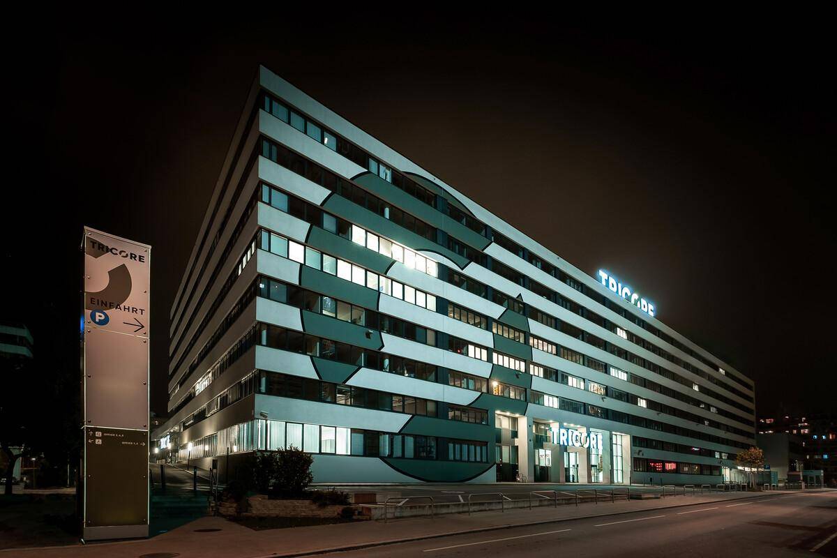 Das moderne Bürogebäude bei Nacht, beleuchtet mit vielen Fenstern und einem markanten Eingangsbereich.