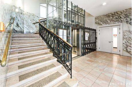 Elegante Lobby mit Marmorwänden, Steintreppe und einem kunstvollen Glasaufzug.