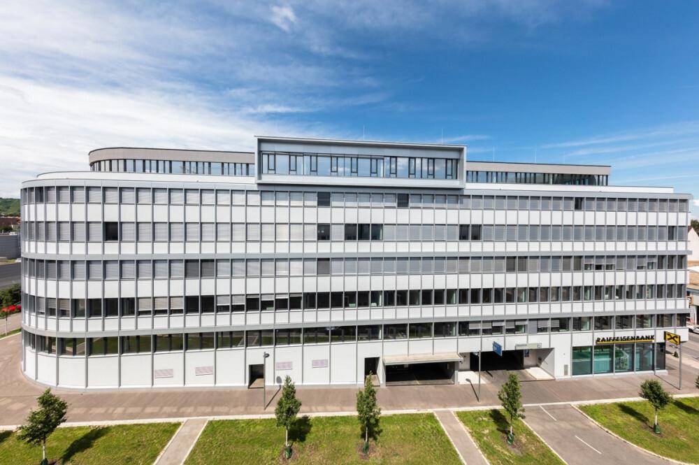 Großes, modernes Bürogebäude mit vielen Fenstern und einer geschwungenen Fassade unter blauem Himmel.