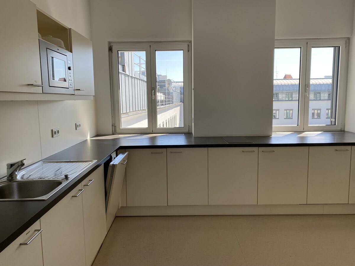 Moderne Einbauküche mit weißen Schränken, dunkler Arbeitsplatte und Fenstern mit Blick auf die Stadt.