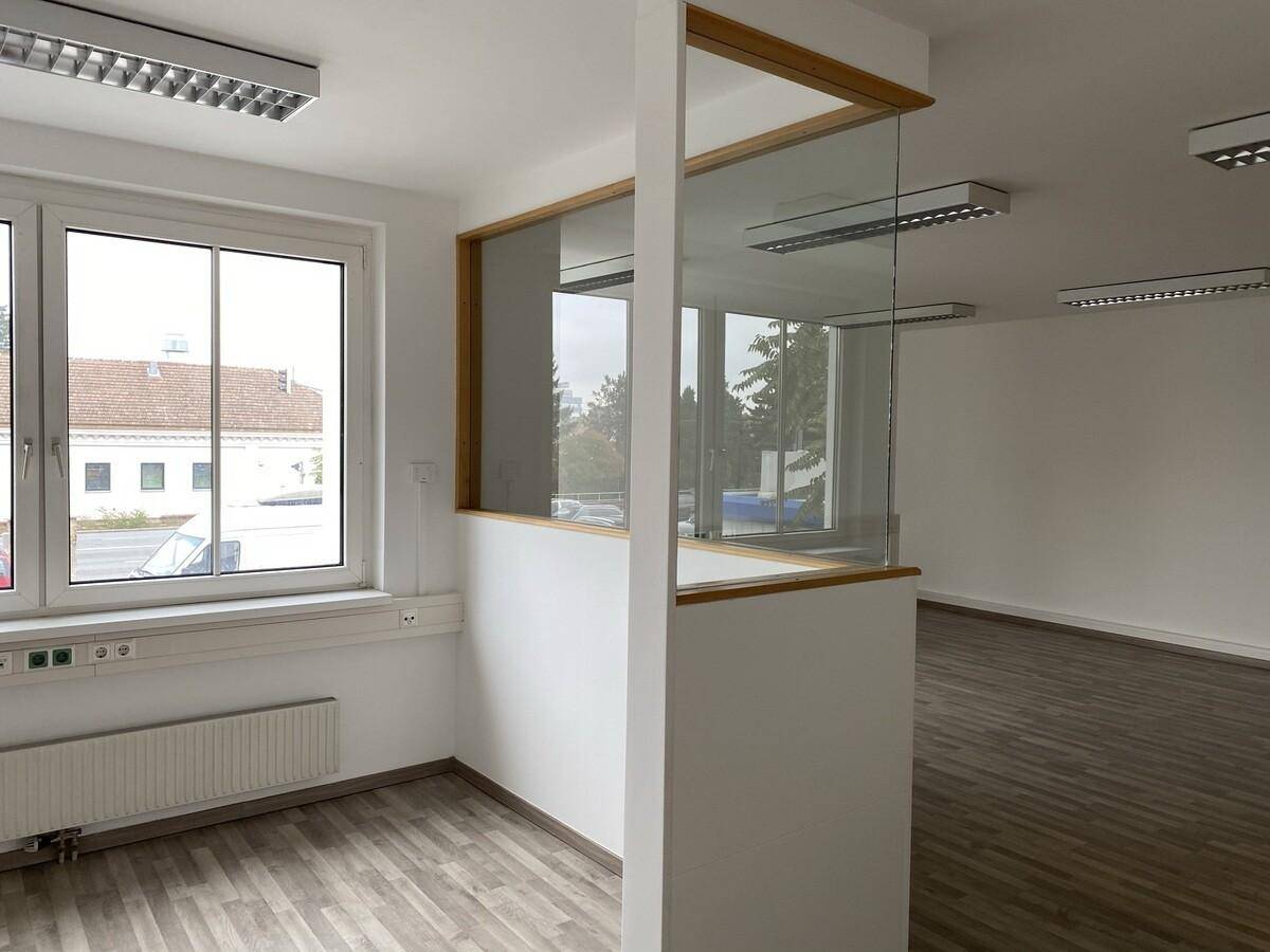 Offener Bürobereich mit Glasabtrennung, Holzparkettboden und großen Fenstern für viel Tageslicht.