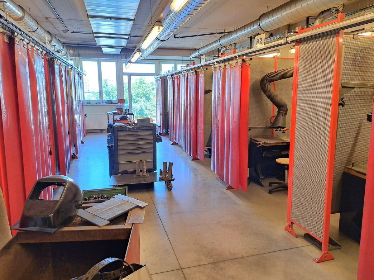 Industrielle Werkstatt oder Schulungsraum mit mehreren Arbeitskabinen und sichtbaren Lüftungsrohren.