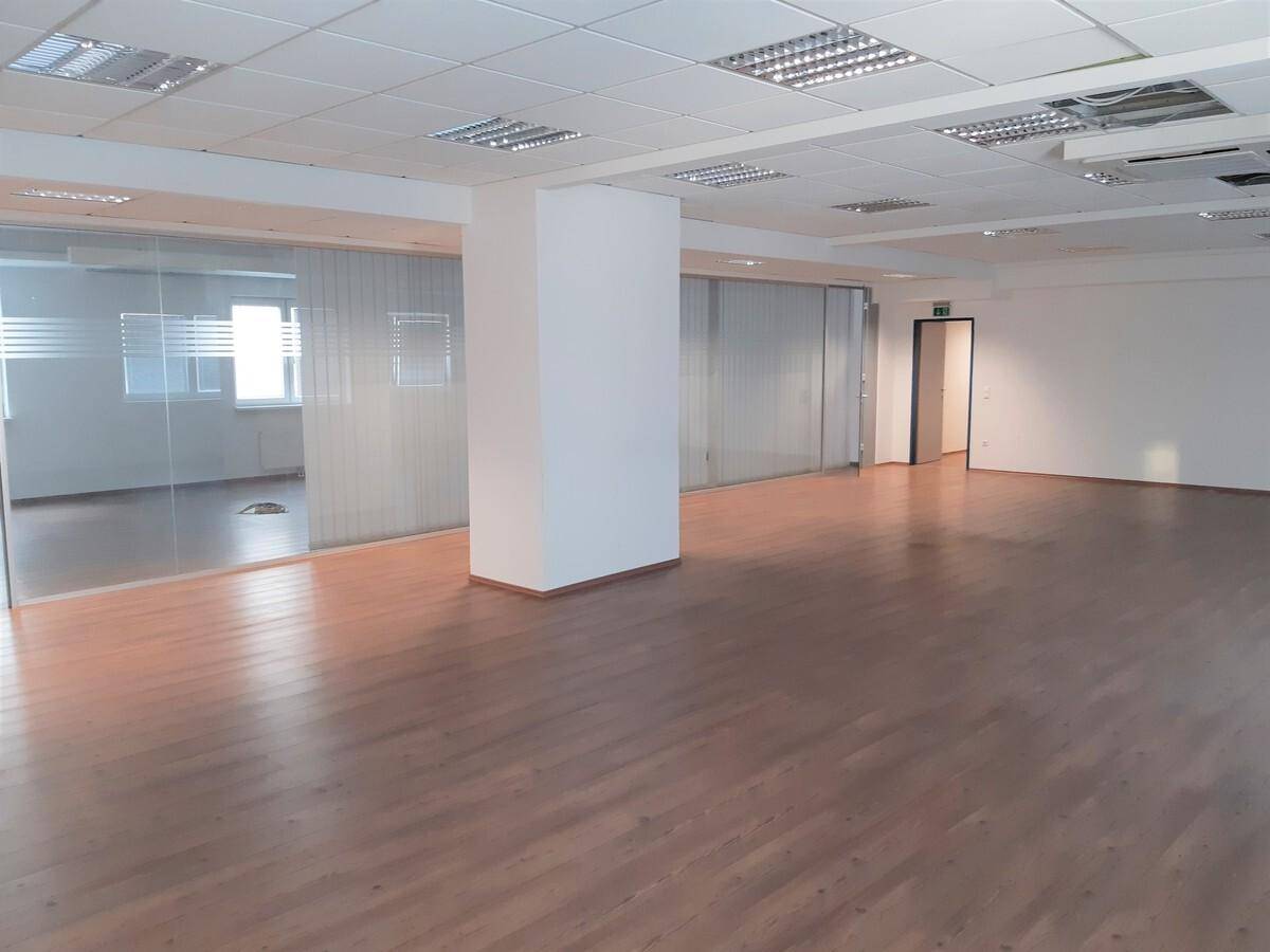 Geräumiger, offener Bürobereich mit Holzfußboden, Glaswänden und abgehängter Decke mit Beleuchtung.