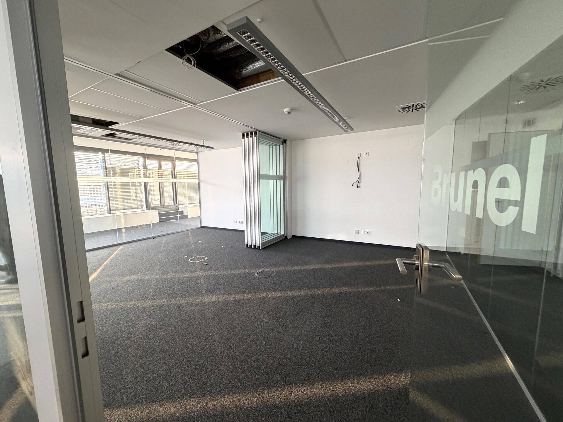 Großes, leeres Büro mit Teppichboden und Glaswänden, bereit für die individuelle Gestaltung und Nutzung.