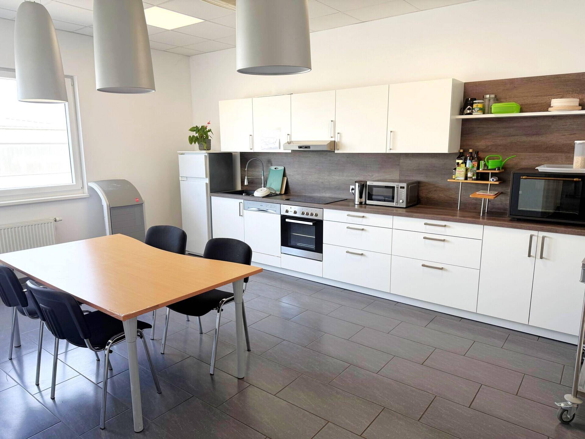 Moderne Teeküche mit weißen Schränken, Esstisch und grauen Fliesenböden.