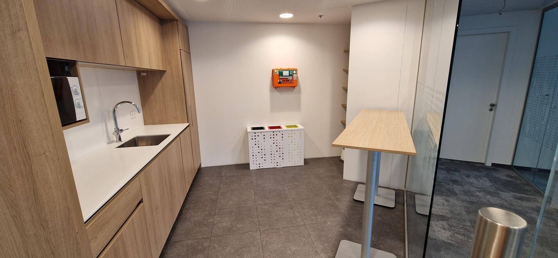 Kleine Teeküche mit Holzschränken, Spüle und Mikrowelle, ideal für Büropausen.