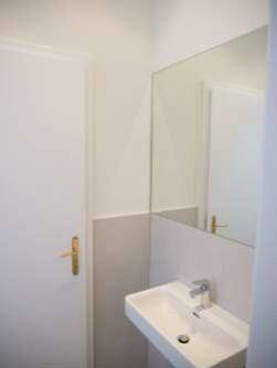Kleines, modernes Badezimmer mit wandmontiertem Waschbecken und großem Spiegel in hellen Farbtönen.