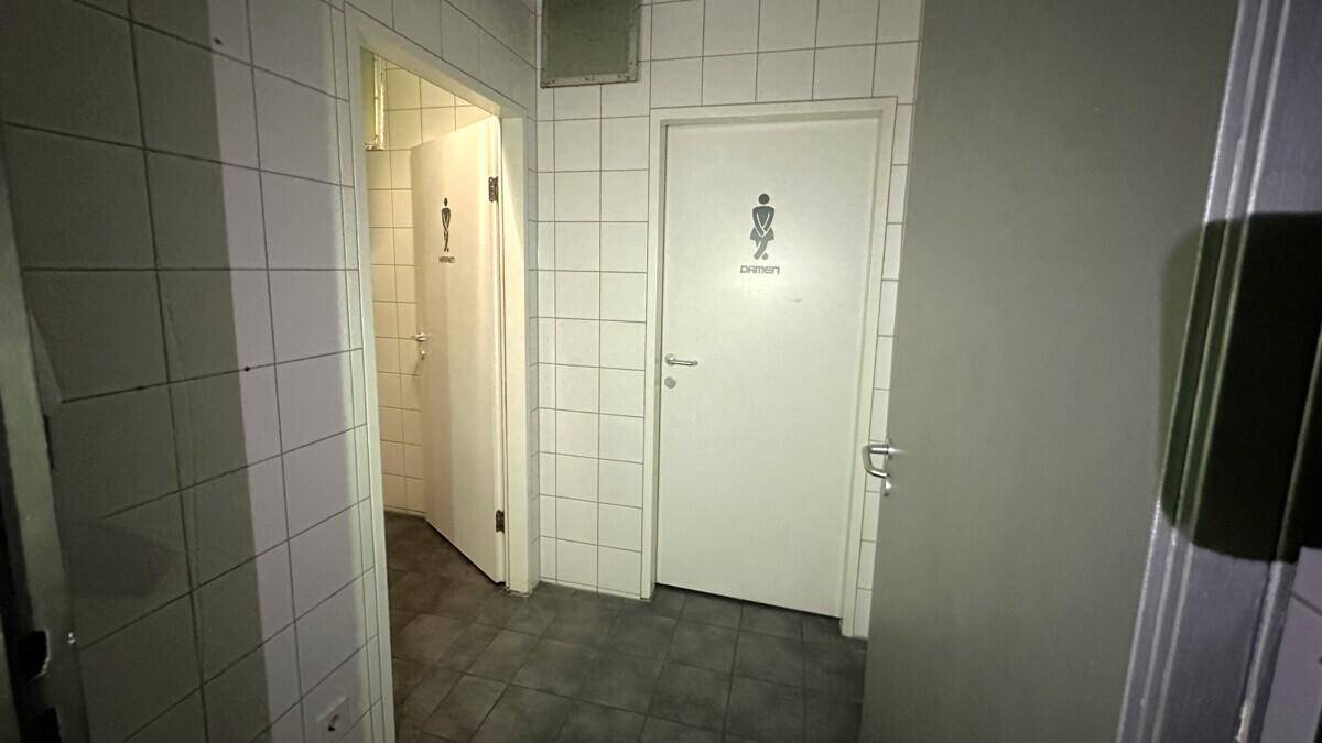 Eingangsbereich zu öffentlichen Toiletten mit weißen Fliesen und Beschilderung für Damen und Herren.