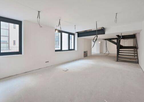 Weitläufiger Gewerberaum mit mehreren Fenstern, Betonboden und Blick auf die Treppe.
