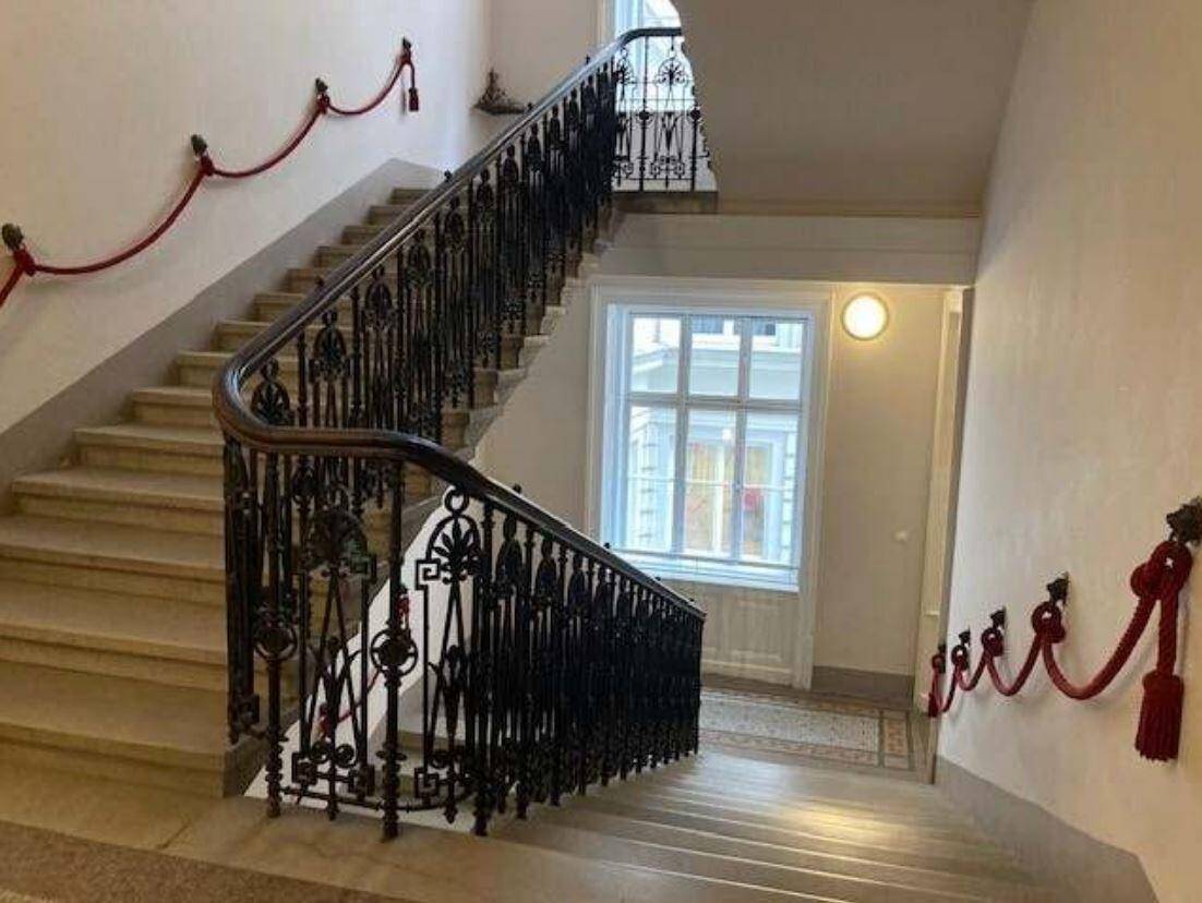 Geschwungenes Treppenhaus mit schmiedeeisernem Geländer, rotem Seilhandlauf und einem großen Fenster für Tageslicht.