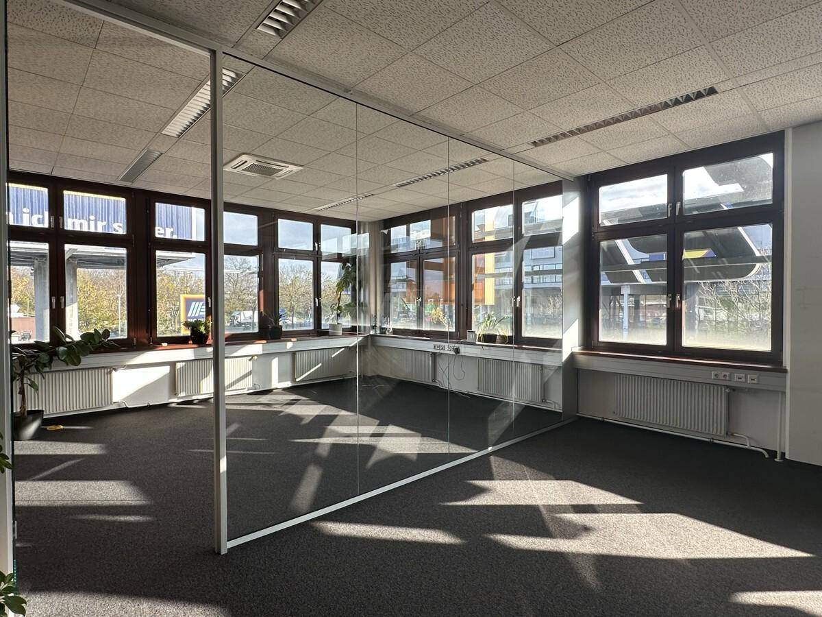 Modernes Büro mit Glaswänden, Teppichboden und viel Tageslicht durch die großen Fenster, ideal für eine offene Arbeitsumgebung.
