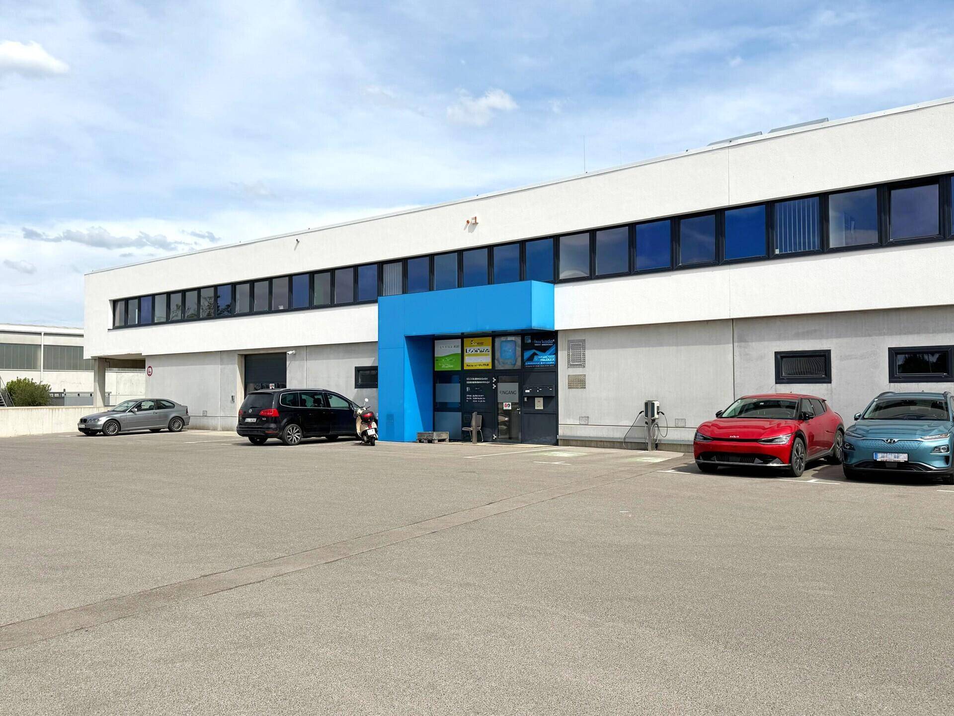 Modernes Geschäftsgebäude mit Parkplätzen und Ladesäulen unter blauem Himmel.