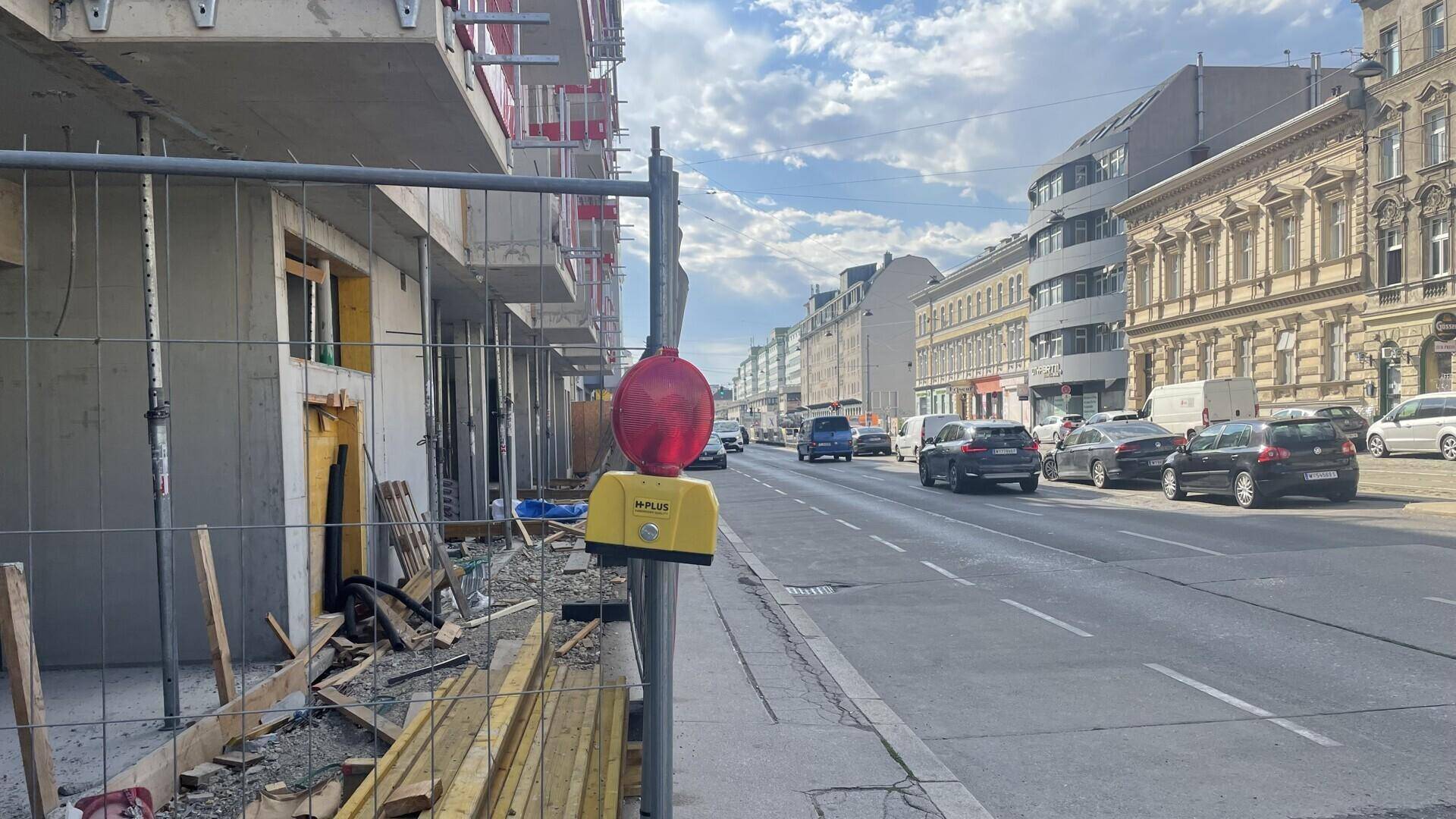 Straßenansicht mit einer Baustelle auf der linken Seite und einer belebten Straße mit Gebäuden auf der rechten Seite.