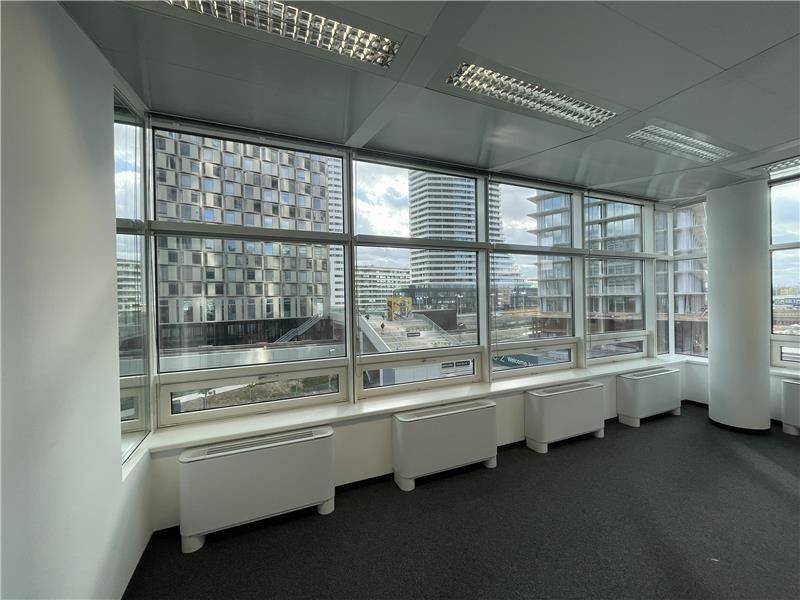 Helles Büro mit Teppichboden und einer Fensterfront, die einen weiten Blick auf die umliegende Stadtlandschaft ermöglicht.