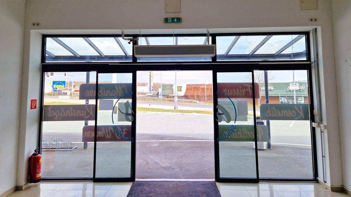 Blick vom Eingangsbereich eines Geschäfts nach draußen auf den Parkplatz und weitere Gebäude.