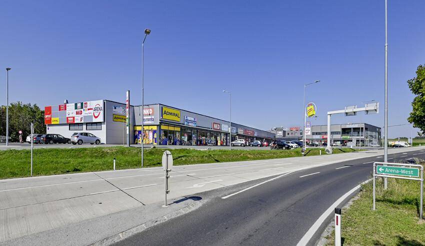 Weitläufiges Einkaufszentrum mit verschiedenen Geschäften und einem Parkplatz entlang einer Straße.