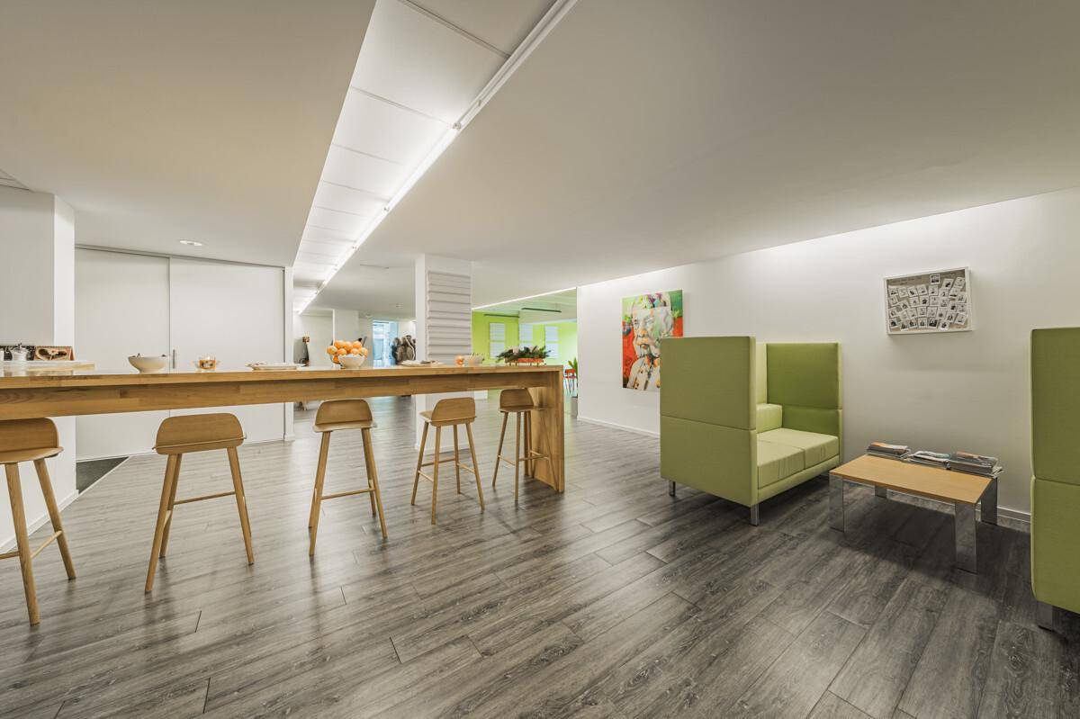 Gemütlicher Loungebereich mit Holztresen, Barhockern und grünen Sitzgelegenheiten auf modernem Vinylboden.