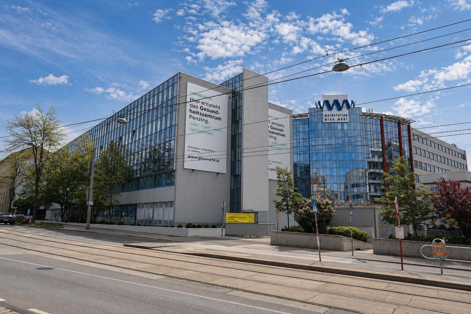 Gebäudeansicht von der Straße mit Straßenbahnschienen im Vordergrund und Glasfassade.