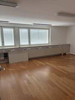 Heller Büroraum mit Holzboden, großen Fenstern und einer langen Reihe von integrierten Schränken.