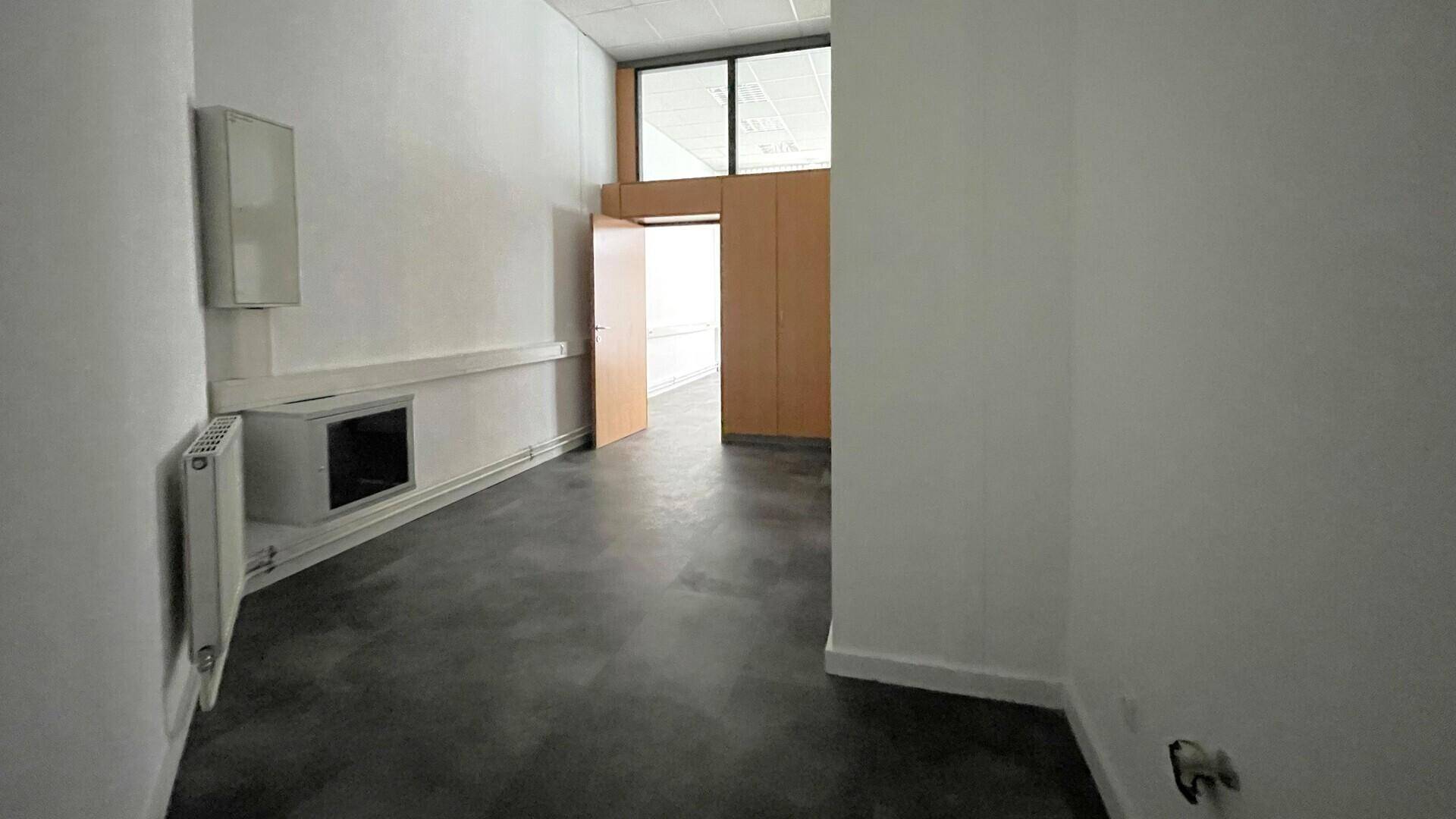 Leerer Bürobereich mit dunklem Boden, weißen Wänden und einem Blick durch eine offene Tür in einen weiteren Raum.