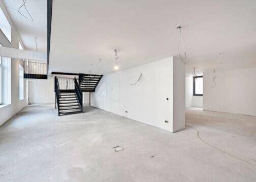 Weitläufiger, heller Gewerberaum mit Betonboden und einer markanten schwarzen Treppe zu einer Galerie.
