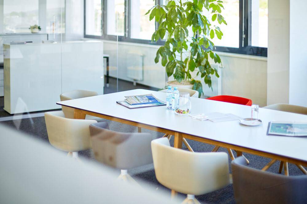 Heller Besprechungsraum mit großem Tisch, modernen Stühlen und viel Tageslicht durch die Fenster.