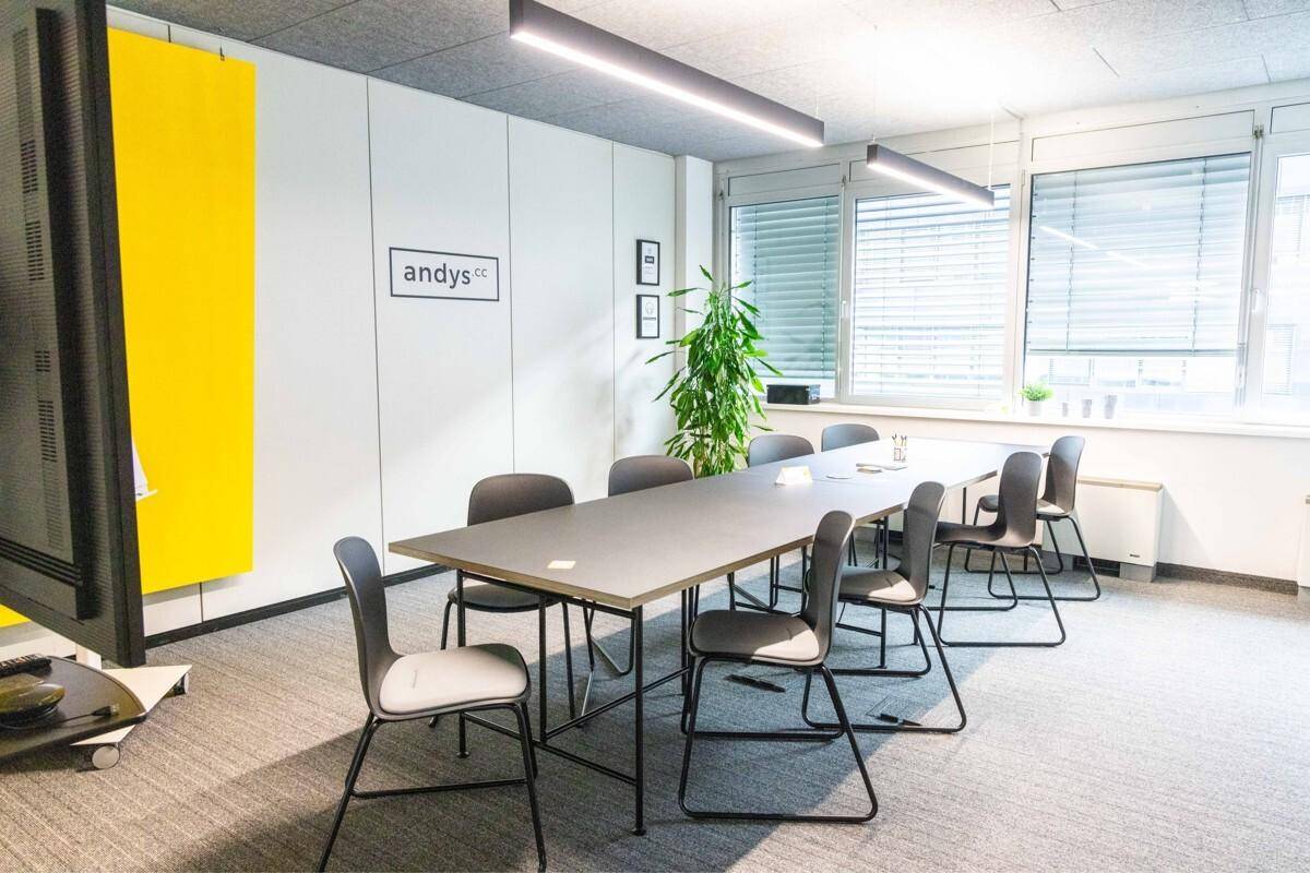 Heller Konferenzraum mit großem Tisch, bequemen Stühlen und großen Fenstern für viel Tageslicht.