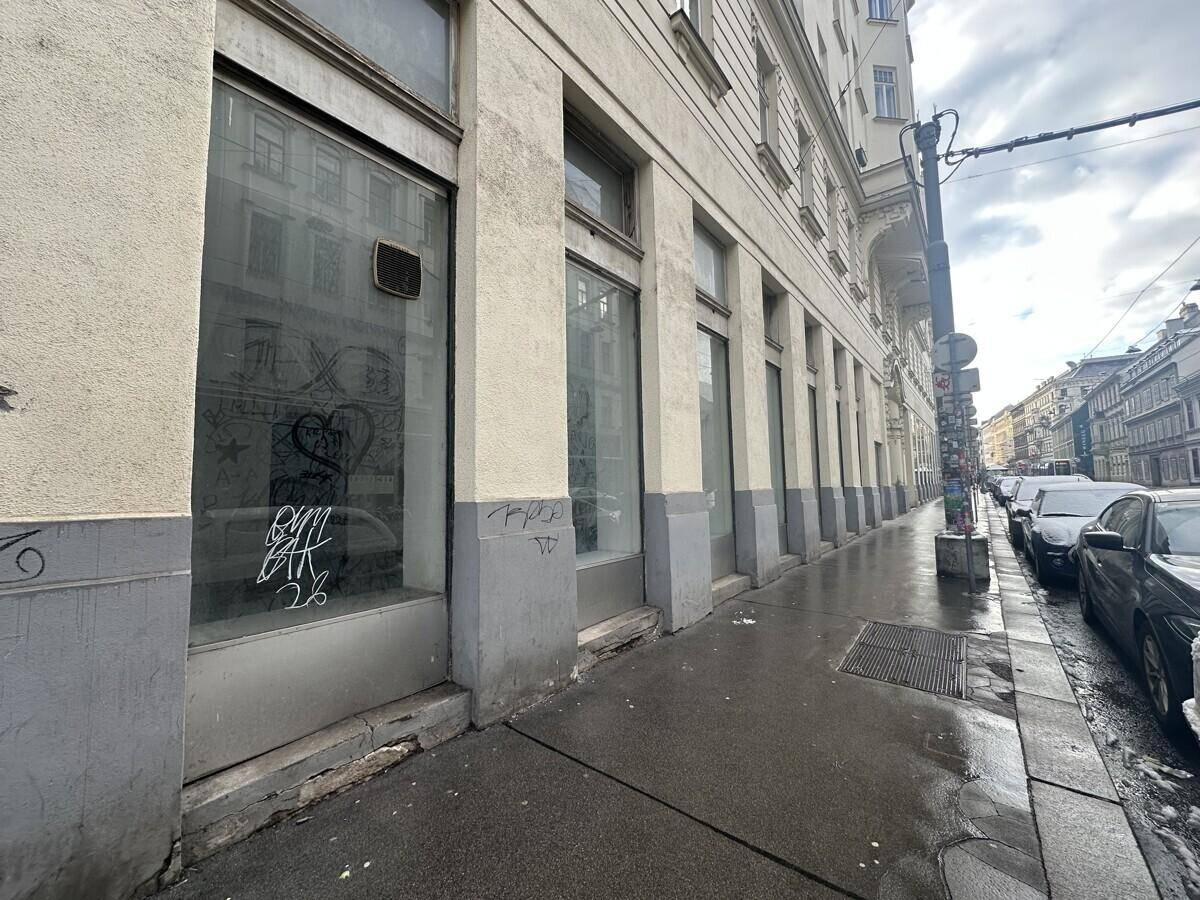 Die Fassade eines Gebäudes mit großen Schaufenstern, die teilweise mit Graffiti versehen sind, an einer städtischen Straße.