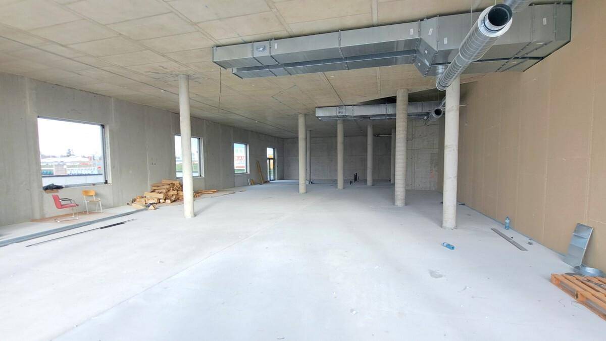 Großer, unfertiger Gewerberaum mit Betonwänden, kleineren Fenstern und sichtbaren Lüftungsrohren an der Decke.