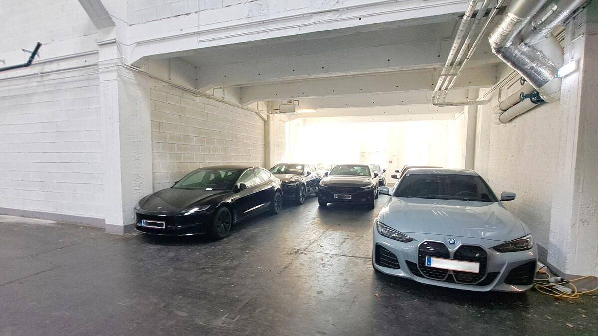 Innenbereich einer Parkgarage mit mehreren Autos und sichtbaren Rohrleitungen an der Decke.
