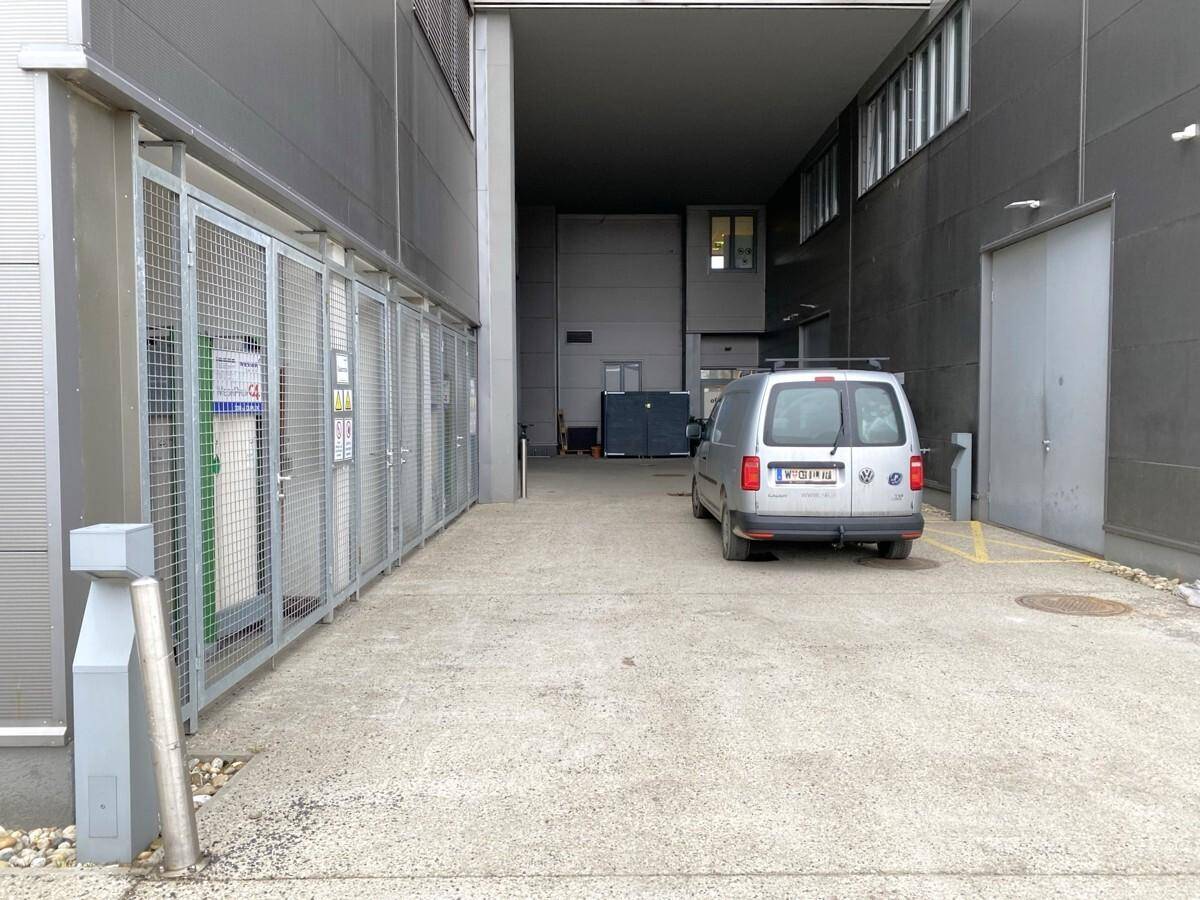 Schmale Zufahrt oder Gasse neben einem Gebäude mit einem geparkten Lieferwagen und Gitterzäunen.