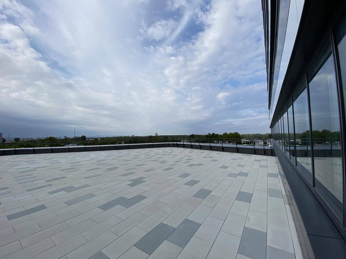 Weitläufige Dachterrasse mit modernem Fliesenmuster und Blick auf die Umgebung unter bewölktem Himmel.