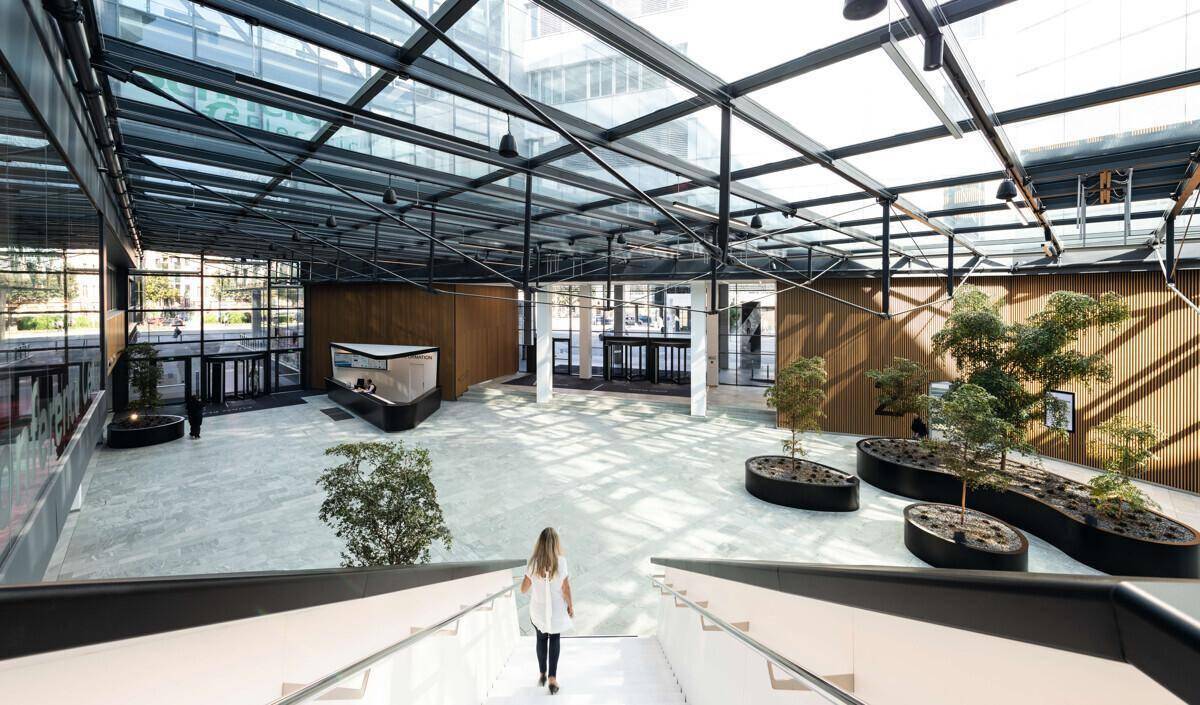 Großzügiges Atrium mit Glasdach, modernen Pflanzenkübeln und heller Steinbodenfläche.