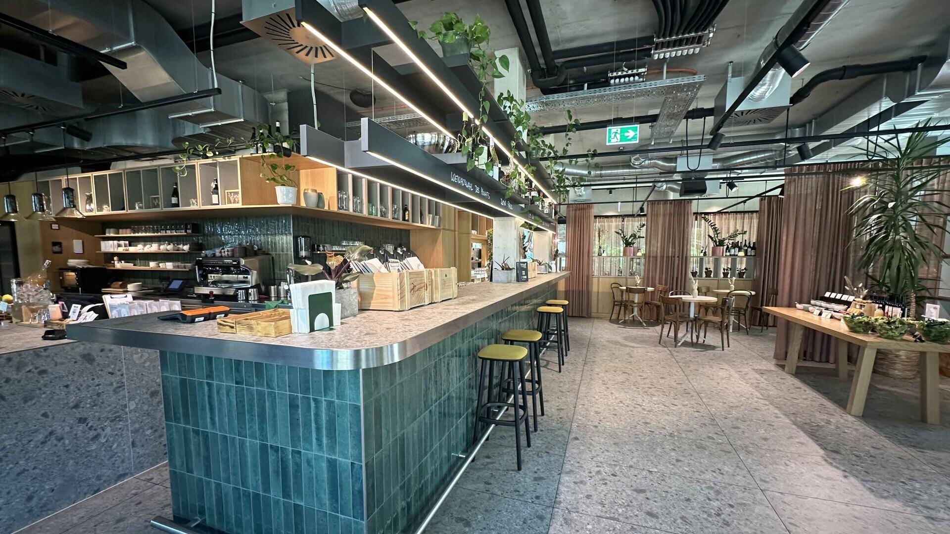 Lange Bar mit grünen Fliesen, Barhockern und offener Deckenkonstruktion in einem modernen Ambiente.