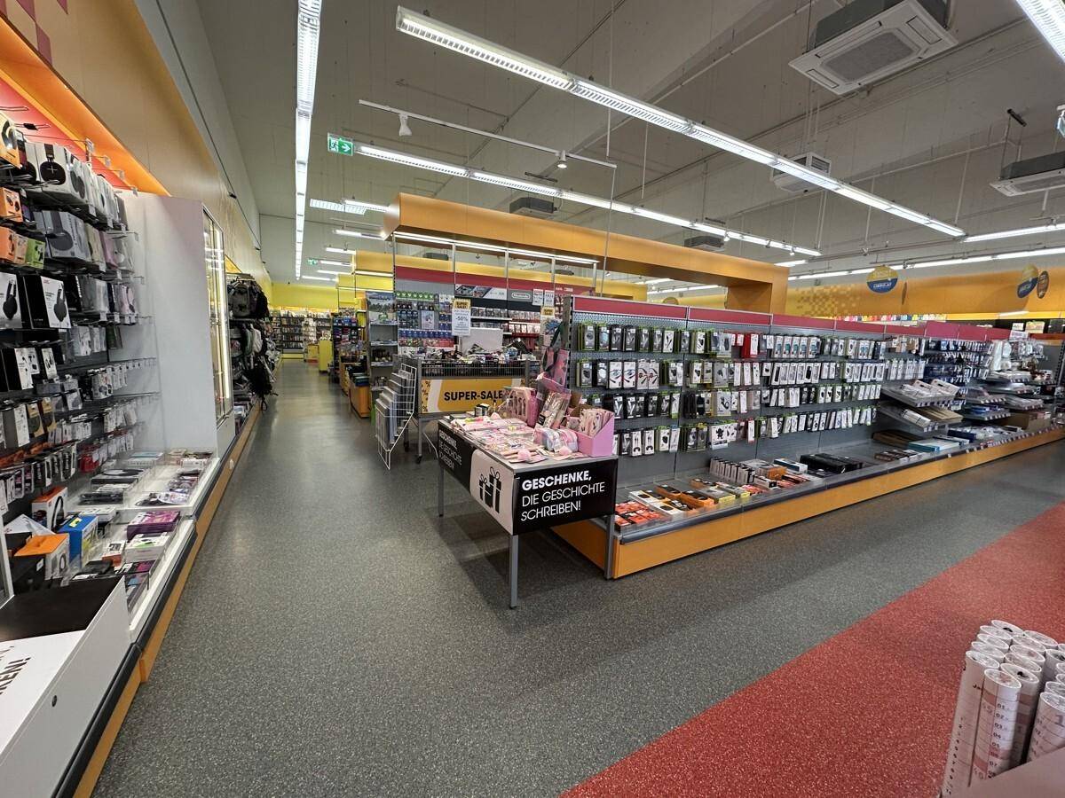 Langer Gang in einem Einzelhandelsgeschäft mit Regalen voller Produkte und heller Deckenbeleuchtung.