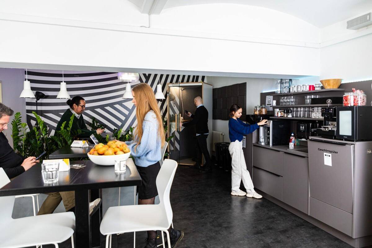 Moderne Büroküche mit Kaffeemaschine und Geschirrspüler, genutzt von Mitarbeitern in einem lebhaften Ambiente.