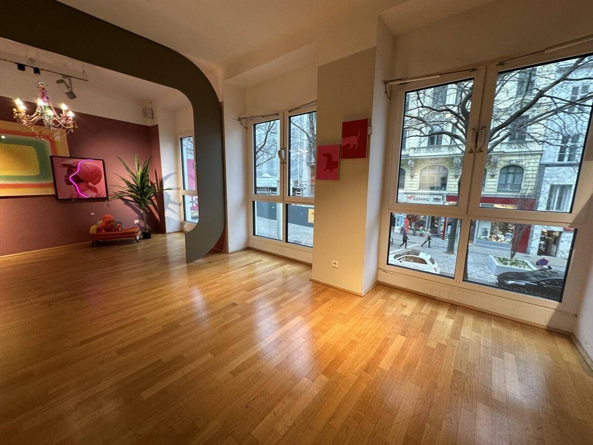 Heller Verkaufsraum mit großen Fenstern zur Straße, Holzboden und moderner Einrichtung.