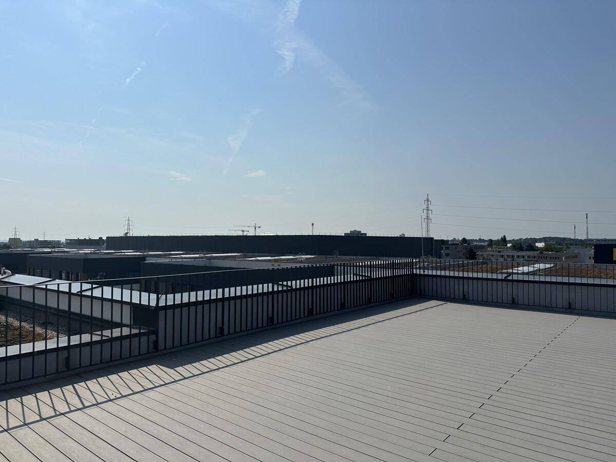 Weitläufige Dachterrasse mit Metallgeländer und Blick auf die umliegende Bebauung und den Himmel.