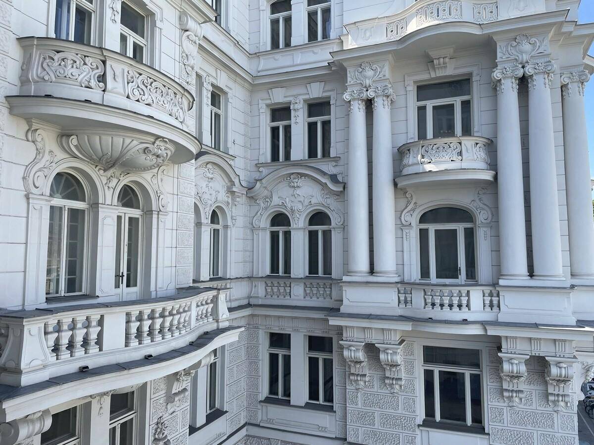 Detailansicht der reich verzierten weißen Fassade eines Altbaus mit mehreren Balkonen und klassischen Säulen.