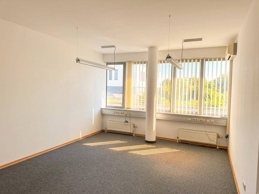 Helles Büro mit Teppichboden, großen Fenstern, Klimaanlage und einem zentralen Pfeiler.