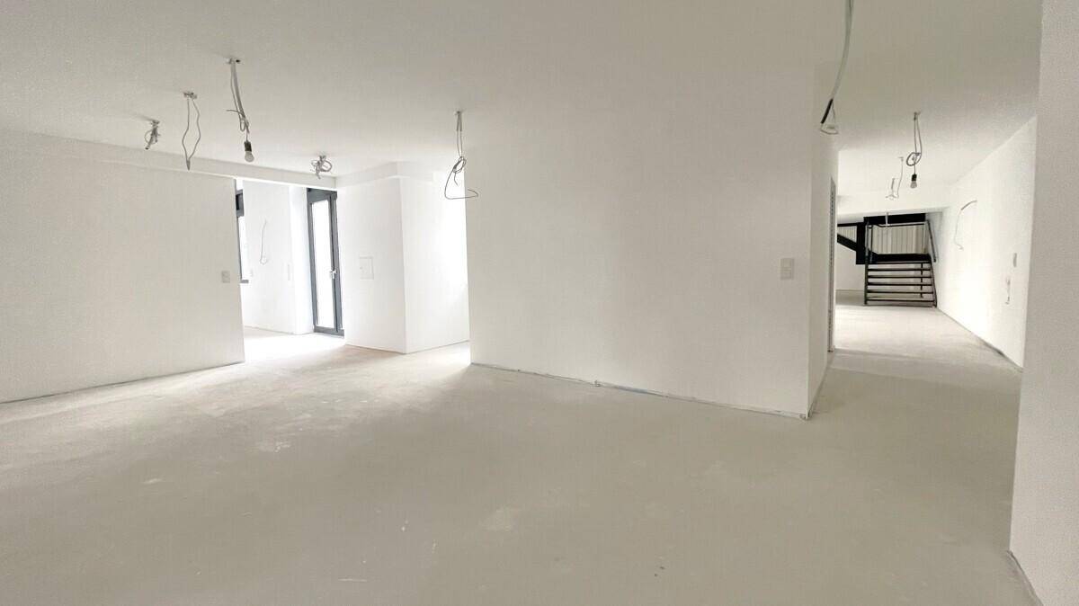 Weitläufiger, heller Raum mit Betonboden und weißen Wänden, bereit für den Innenausbau.