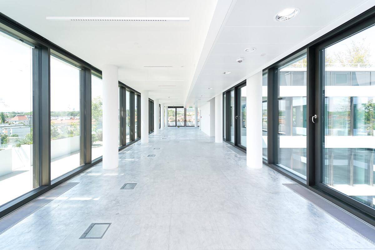 Heller, leerer Büroflur mit großen Fenstern, die viel Tageslicht hereinlassen und einen weiten Blick bieten.