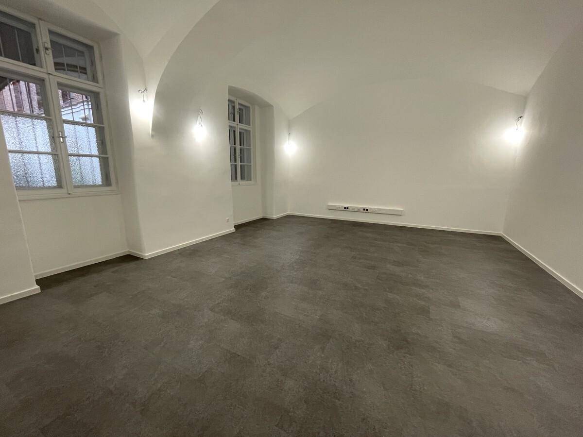 Heller Raum mit einer charakteristischen Gewölbedecke, weiß gestrichenen Wänden und modernem dunklem Bodenbelag, ideal für verschiedene Nutzungen.